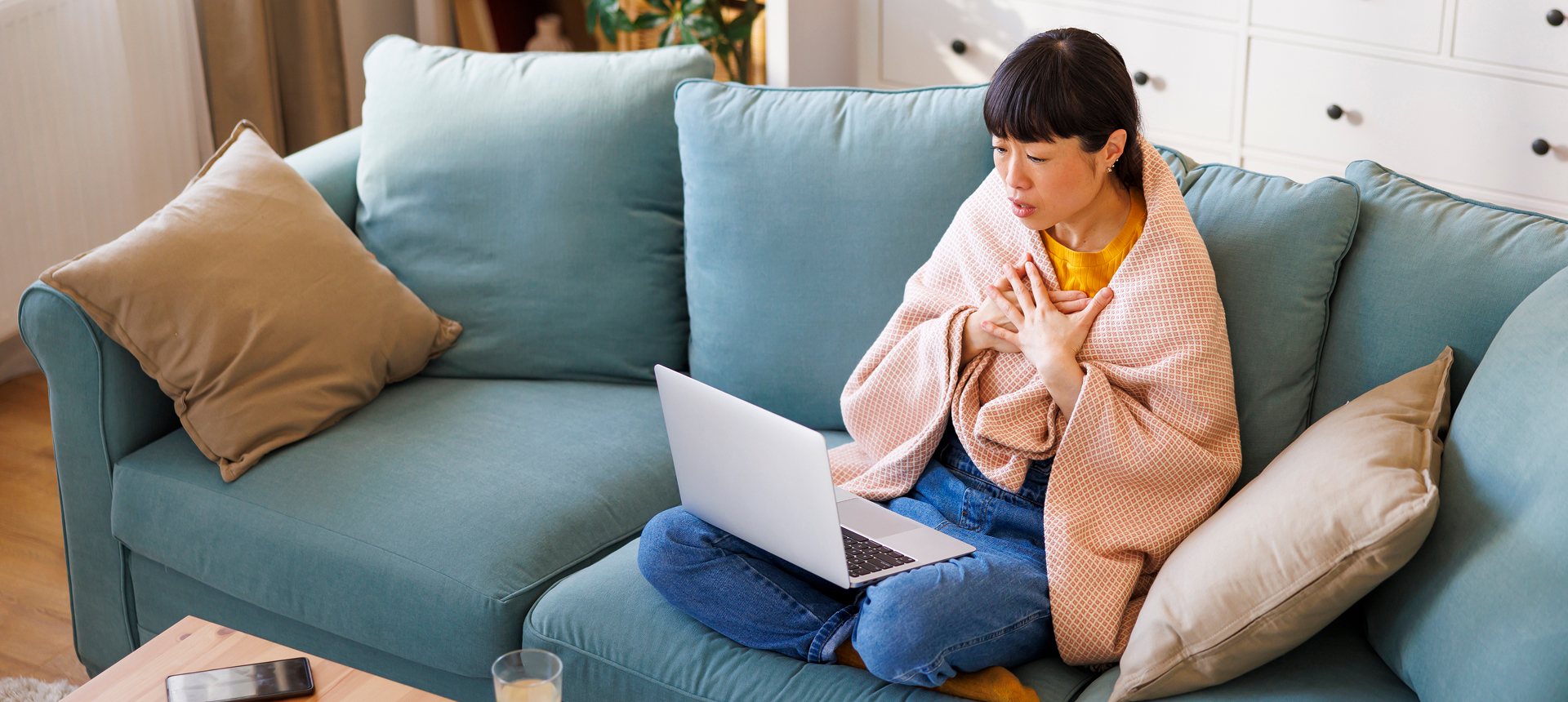 Woman wrapped in blanket using laptop on sofa