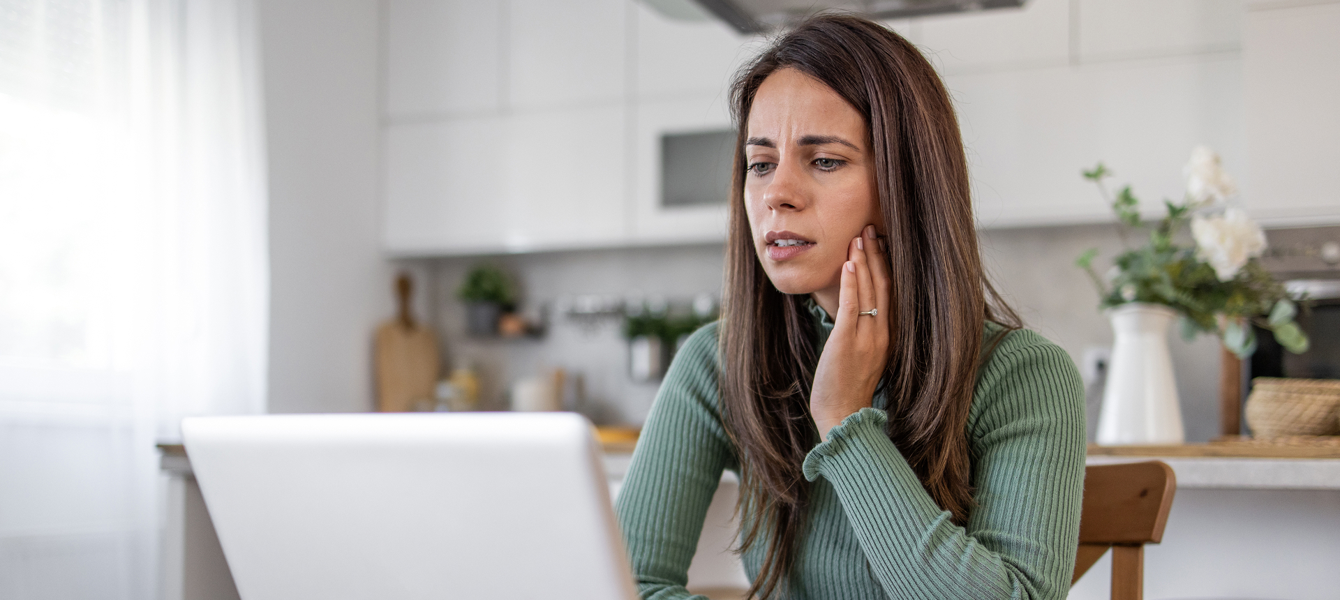 Woman in kitchen looking concerned at laptop