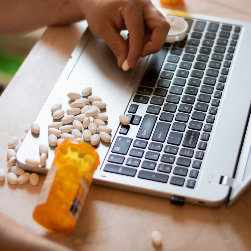 Open pill bottle near laptop keys