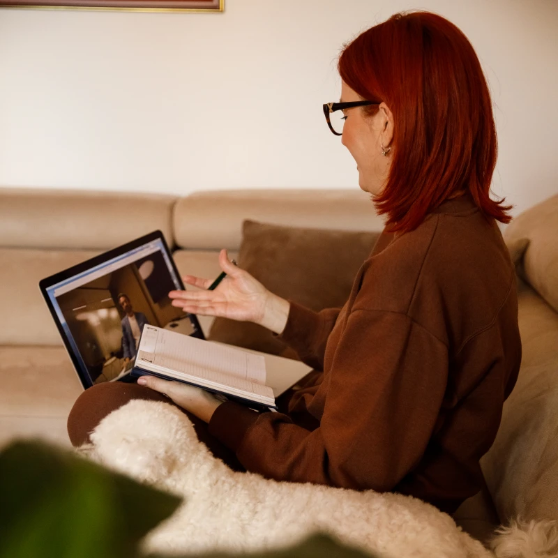 Person taking notes during virtual call on couch